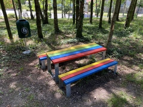 Holzbänke und Tisch in Regenbogenfarben für Kleinkinder unter den Bäumen im Schatten