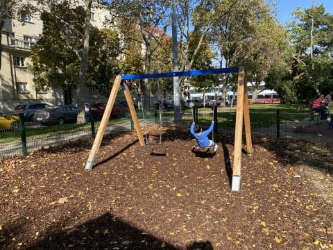Doppelschaukel mit blauem Balken auf Kinderspielplatz und Rindenmulch Boden