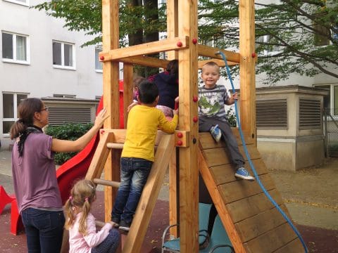 Kinder am Spielplatz auf Spielturm mit schräger Kletterwand