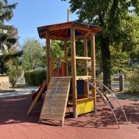 Turmanlage auf Kinderspielplatz mit schräger Rampe mit Seil und roter Rutsche auf rotem Fallschutz