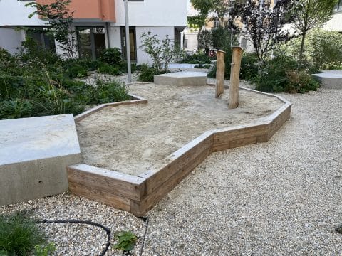 Sonderform Sandkasten aus Lärchenholz in einem begrünten Hof