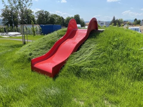 Hangrutsche Breit in Rot auf einem mit Rasen bewachsenen Hügel