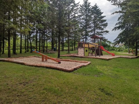 Waldspielplatz mit Doppelwippe im Sandkasten und Spielturm mit Rutsche