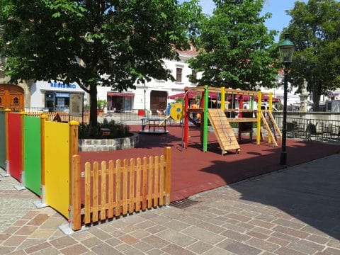 Spielplatz in der Fußgängerzone mit Holzzaun unter Bäumen