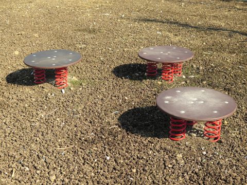 3 runde Hüpfplatten aus Holz mit je drei roten Federn im Boden verankert