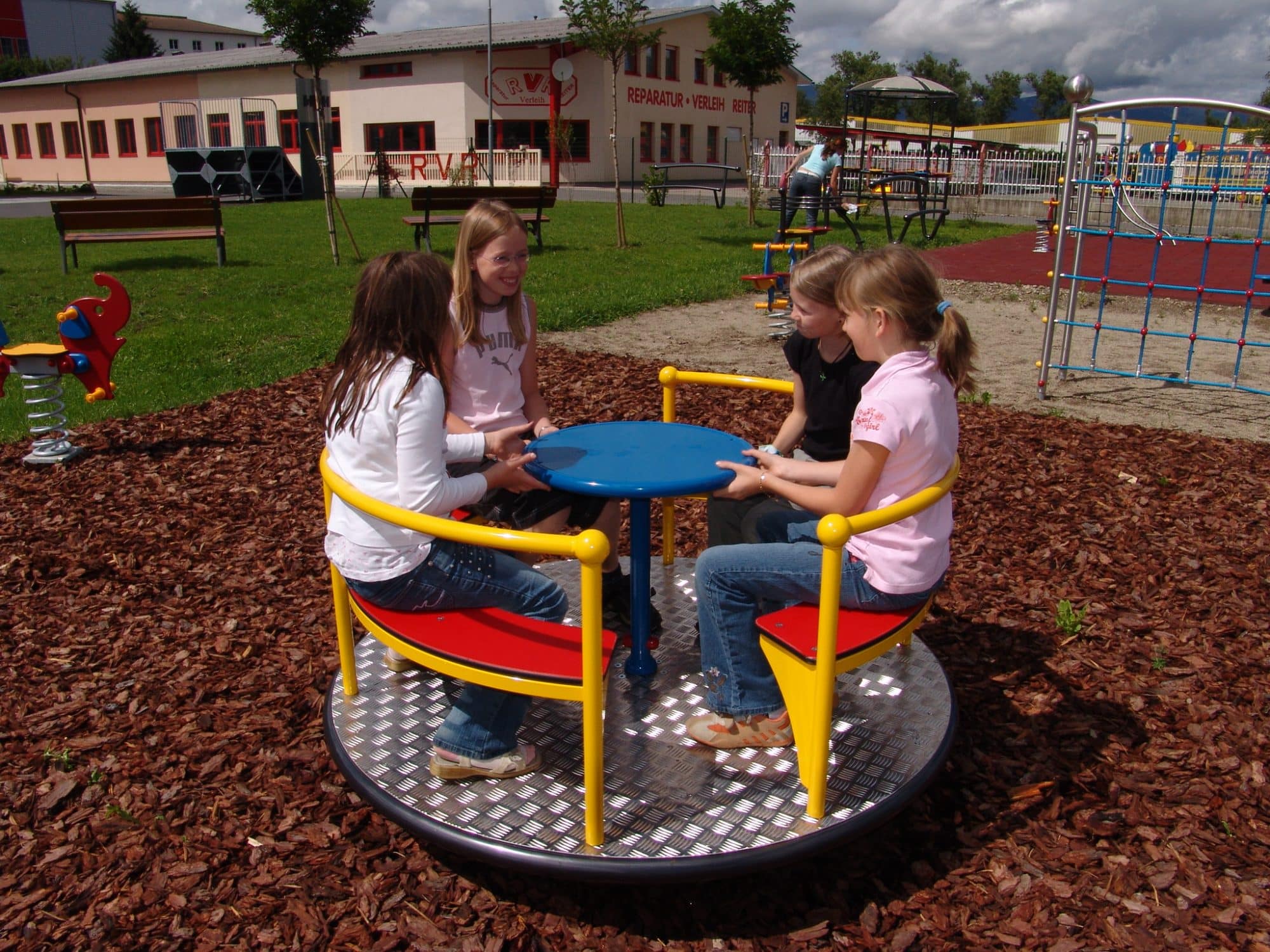 Kinder auf Sitzkarussell auf dem Spielplatz auf Rindenmulch
