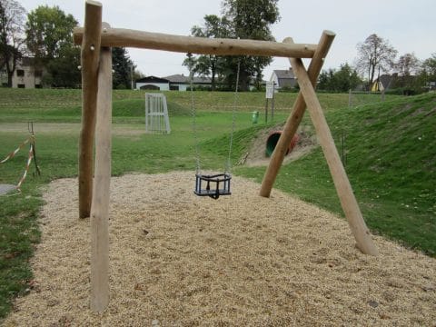 Einfachschaukel Kleinkindersitz an Holzpalisaden auf dem Spielplatz