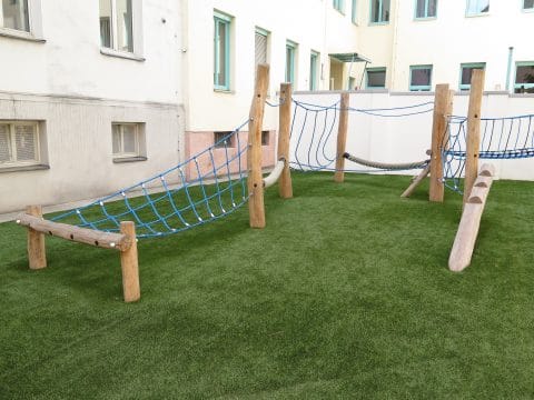 Spielgeräte für Kinder bei Wohnhausanlage mit blauen Netzen und Holz zum balancieren