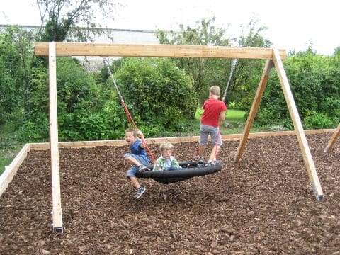 Drei Kinder spielen am Spielplatz auf Nestschaukel