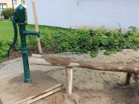 Sand-Wasser-Spiel mit grüner Wasserpumpe im Sandkasten