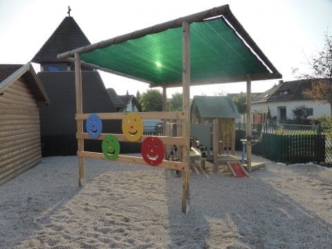 Kinderspielplatz im Sand mit Sonnensegen an der Kirche