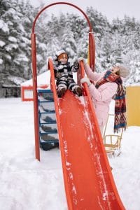 Spielplatz mit Kind und Mutter im Schnee